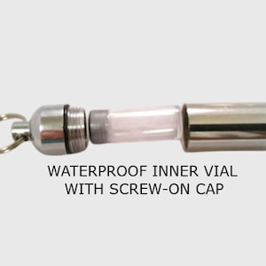 May include: A silver-colored waterproof vial with a screw-on cap and a keyring attachment. The vial has a clear, cylindrical inner chamber. The text "WATERPROOF INNER VIAL WITH SCREW-ON CAP" is printed below the vial.
