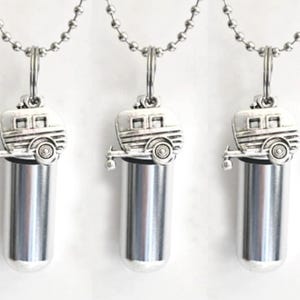 May include: Five silver-colored pendant necklaces. Each necklace features a small, cylindrical vial suspended beneath a detailed, silver-toned charm shaped like a vintage camper trailer. The pendants hang from a ball chain.
