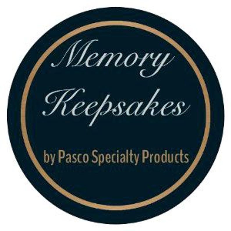 Pode incluir: Um log&oacute;tipo circular com um fundo azul-marinho escuro e uma borda dourada fina. O texto Memory Keepsakes est&aacute; escrito numa fonte cursiva branca, e o texto by Pasco Specialty Products est&aacute; escrito numa fonte sans-serif branca mais pequena.