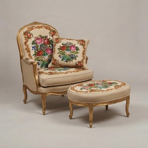 Könnte beinhalten: Ein Sessel und ein passender Hocker mit goldfarbenen Holzrahmen. Der beigefarbene Bezug ist mit farbenfrohen floralen Stickmustern auf der Sitzfläche, der Rückenlehne und dem Hocker versehen. Ein quadratisches Kissen mit passendem Blumenmuster liegt bei.
