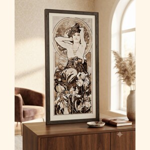 May include: A vertical framed wall art piece featuring a sepia-toned illustration of a figure with arms raised behind their head, positioned above a cluster of iris flowers. The artwork is enclosed in a dark brown rectangular frame with a white mat.