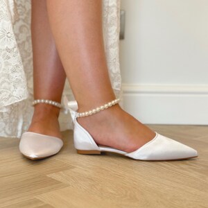 Pu&ograve; includere: Scarpe da sposa in raso bianco con cinturino alla caviglia di perle e punta a punta.