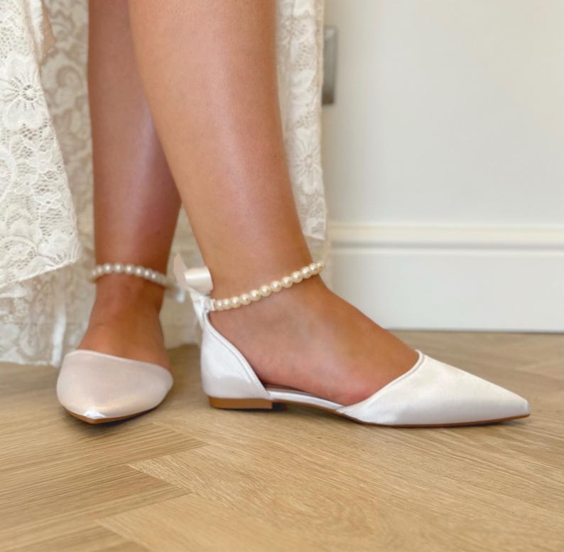 Pu&ograve; includere: Scarpe da sposa in raso bianco con cinturino alla caviglia di perle e punta a punta.