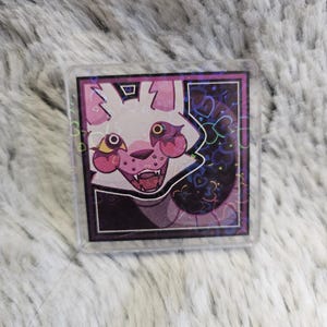 Può includere: Un personaggio dei cartoni animati bianco e rosa con occhi gialli e una bocca spalancata. Il personaggio è circondato da uno sfondo viola e nero con cuori e stelle. L'immagine è stampata su un portachiavi in ​​acrilico trasparente.