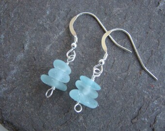 May include: A pair of silver earrings with light blue sea glass beads. The earrings are made with a simple hook design.