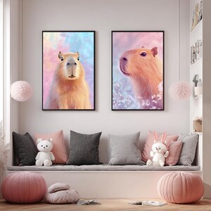 May include: Two framed art prints featuring capybaras. One shows a front-facing capybara against a pastel background, the other a side profile. The artwork has a soft, painterly style with warm tones and black frames.