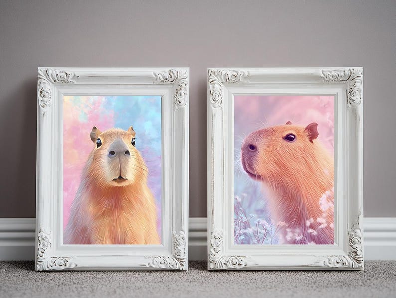 May include: Two framed art prints featuring capybaras. One print shows a capybara facing forward against a colorful background. The other print shows a capybara in profile with a soft pink and blue background. Both are in white ornate frames.