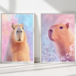 May include: Two framed art prints featuring capybaras. One print shows a capybara facing forward against a pastel blue and pink background. The other print depicts a capybara in profile with a pink and blue backdrop.