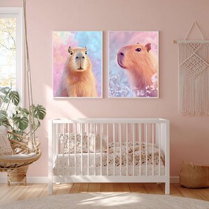 May include: Two framed art prints featuring capybaras. One print shows a capybara facing forward against a pastel background of pink, blue, and yellow. The other print shows a capybara in profile against a similar background. The prints are above a white crib.