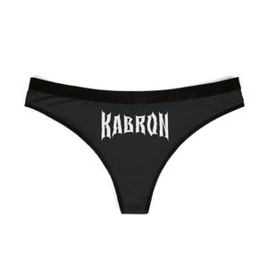 Könnte beinhalten: Schwarzer Slip mit dem weißen Schriftzug "KABRON" in gotischer Schrift. Die Unterwäsche hat einen schwarzen Bund und Besatz.