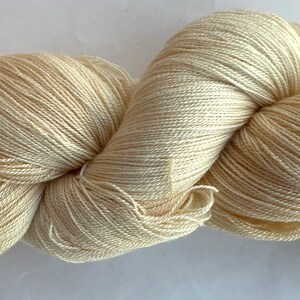 May include: A skein of off-white yarn, tightly wound and twisted, creating a textured appearance. The yarn appears soft and is likely intended for knitting or crocheting projects. The color is a creamy, neutral tone.