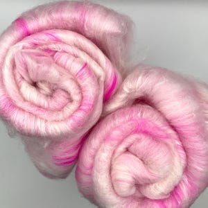 May include: Two rolls of pink and white fluffy yarn with pink highlights. The yarn is rolled up and ready to be used for knitting or crocheting.
