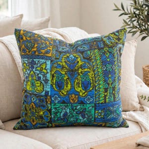 Peut inclure: Un coussin carré présentant un motif patchwork vibrant avec des dessins floraux et géométriques complexes dans des tons de bleu profond, de vert citron vif et de jaune doré. Le tissu affiche un motif répétitif sur plusieurs panneaux rectangulaires.
