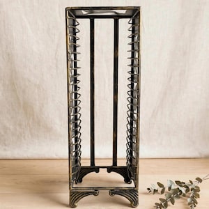 May include: A tall, rectangular metal storage rack with a distressed black and gold finish. The structure features vertical side panels with evenly spaced horizontal wire slots designed for organizing media cases, supported by four ornate feet.