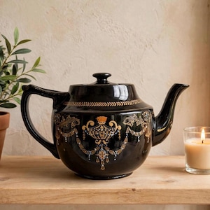 Peut inclure: Une théière en céramique noire brillante ornée d'un motif néoclassique doré avec des guirlandes, des urnes et des motifs de feuilles délicats. La théière possède une anse courbée, un couvercle assorti avec un bouton et un bec verseur effilé.