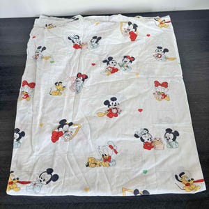 Puede incluir: Sábana blanca con un patrón repetido de Mickey Mouse, Minnie Mouse, Donald Duck y Pluto. Los personajes de dibujos animados están en varias poses, con acentos rojos, amarillos y negros. La sábana es probablemente para una cama infantil.