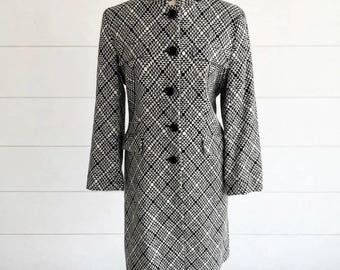 May include: A knee-length coat featuring a high collar and a repeating black and white geometric pattern of concentric squares and circles. The coat has long sleeves, a straight hemline, and a front button closure with five visible black buttons.