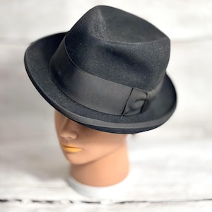 May include: A black fedora hat with a grosgrain ribbon band. The hat is displayed on a mannequin head. The hat has a classic, timeless design.