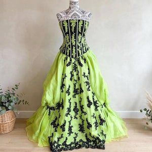 Peut inclure: Une robe de bal sans bretelles avec un corsage vert citron orné de passepoils noirs verticaux et de dentelle florale noire. La jupe ample est vert citron avec des appliques en dentelle noire descendant sur le devant, créant un contraste marqué.