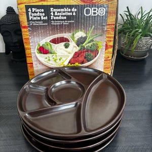 May include: A set of four brown ceramic fondue plates, each with divided sections. The plates are 23 cm in diameter. The box behind the plates reads "4 Piece Fondue Plate Set" and "Fine Ceramic".
