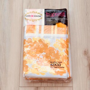 May include: Packaged set of two pillow cases. The pillowcases are white with a floral pattern in shades of orange and yellow. The package reads "42x33" inches and "TEX MADE". The packaging also states "50% Polyester 50% Cotton".