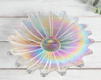 Può includere: Una ciotola in vetro trasparente a forma di fiore con molti petali che si irradiano da una base circolare centrale. Il vetro presenta una finitura iridescente che riflette i colori dell'arcobaleno su tutta la superficie della ciotola.