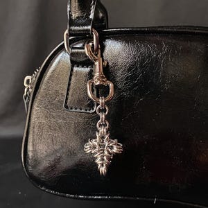 K&ouml;nnte beinhalten: Schwarze Ledertasche mit einer silbernen Kette und einem silbernen Kreuzanh&auml;nger.