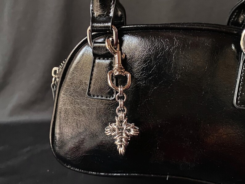 K&ouml;nnte beinhalten: Schwarze Ledertasche mit einer silbernen Kette und einem silbernen Kreuzanh&auml;nger.