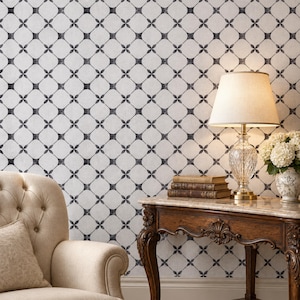 May include: A beige tufted armchair sits beside a dark wood console table with a marble top. On the table, a crystal lamp with a beige shade illuminates a stack of two vintage books and a white ceramic vase filled with white flowers.