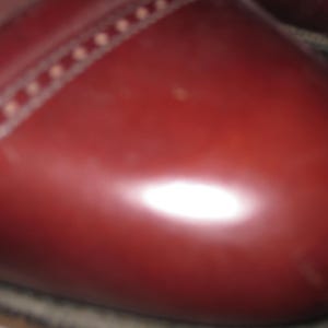 May include: Close-up of a burgundy leather shoe with a stitched seam around the toe.