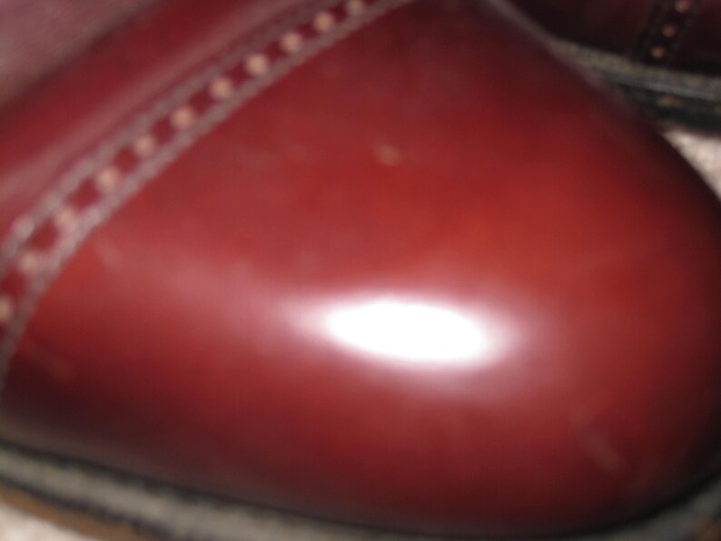 May include: Close-up of a burgundy leather shoe with a stitched seam around the toe.