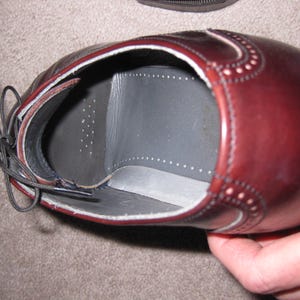 May include: A close-up of the inside of a brown leather oxford shoe. The shoe has a black leather insole with a white stitching detail around the edge.