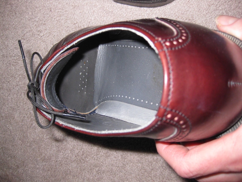 May include: A close-up of the inside of a brown leather oxford shoe. The shoe has a black leather insole with a white stitching detail around the edge.
