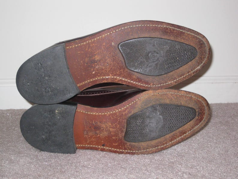 May include: Close-up of the soles of a pair of brown leather shoes. The shoes have a brown leather upper and a black rubber sole.