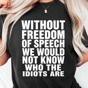 Peut inclure: Un t-shirt noir à manches courtes avec le texte blanc suivant : WITHOUT FREEDOM OF SPEECH WE WOULD NOT KNOW WHO THE IDIOTS ARE. Le vêtement présente une encolure ronde et une coupe standard, avec les lettres majuscules imprimées sur le devant.