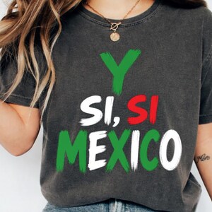 Può includere: Una t-shirt grigio antracite a maniche corte con il testo Y SI, SI MEXICO stampato in stile pennellata. La lettera Y è verde, la parola SI è bianca e rossa, e la parola MEXICO è in verde e bianco, imitando i colori della bandiera messicana.