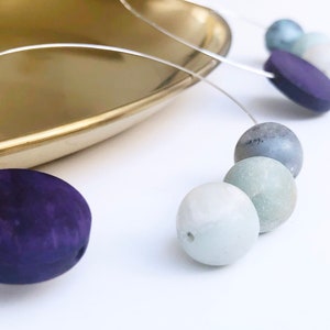 May include: A necklace with a silver chain and a variety of round and oval beads in shades of green, blue, and purple.