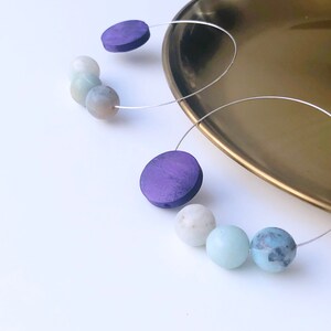 May include: A pair of hoop earrings with purple wooden beads and light blue and white gemstone beads.