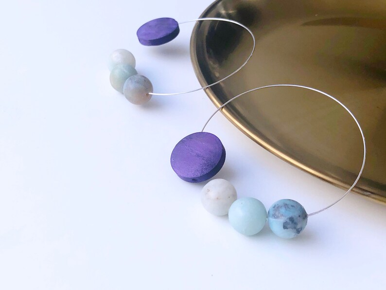 May include: A pair of hoop earrings with purple wooden beads and light blue and white gemstone beads.