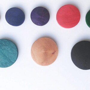 May include: Nine round wooden discs in various colors, including natural wood, dark blue, purple, red, dark green, light green, and black.