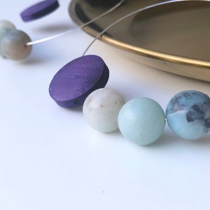 May include: A necklace with purple wooden beads and light blue and green gemstone beads.