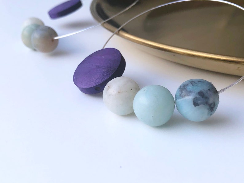 May include: A necklace with purple wooden beads and light blue and green gemstone beads.