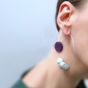 May include: A pair of silver hoop earrings with a purple circle and three white and gray beads hanging from the hoop.