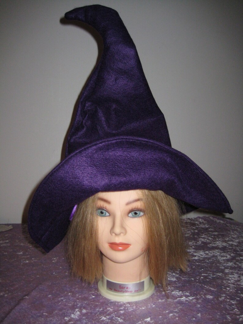 Pu&ograve; includere: Un cappello da strega viola con una corona alta e appuntita e un'ampia tesa. Il cappello &egrave; indossato da un manichino con lunghi capelli biondi.