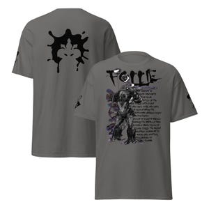 Peut inclure: T-shirt gris foncé avec un motif graphique à l'avant et à l'arrière. Le motif avant comprend le mot "FOLLE" au-dessus d'une illustration et d'un texte. Le dos présente un motif de tache d'encre noire.