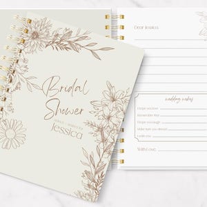 May include: A spiral-bound bridal shower guest book with a floral design. The cover is off-white with the words "Bridal Shower" and "Jessica" in a script font. The open page has lines for wedding wishes.