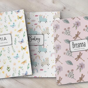 K&ouml;nnte beinhalten: Drei rechteckige Mappen mit personalisierten Etiketten. Die erste ist wei&szlig; mit Schmetterlingen und Blumen, beschriftet mit MIA TAKE HOME FOLDER. Die zweite ist wei&szlig; mit Einh&ouml;rnern und Regenb&ouml;gen, beschriftet mit Bailey HOMEWORK FOLDER. Die dritte ist rosa mit Libellen und Blumen, beschriftet mit Breanna HOMEWORK FOLDER.
