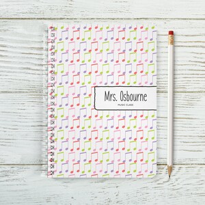 May include: A white spiral notebook with a colourful music note pattern. The notebook has a label that says "Mrs. Osbourne Music Class".