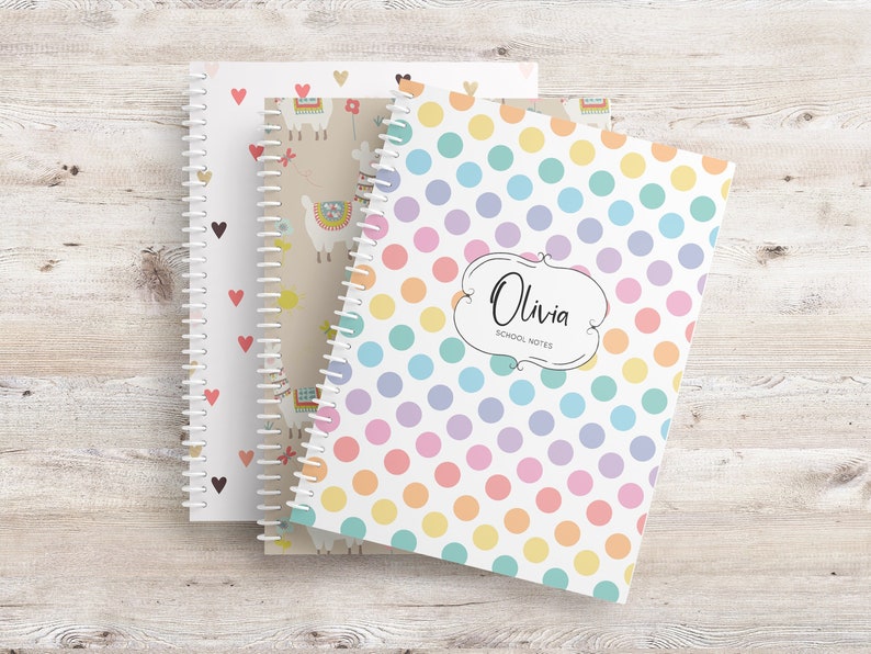 May include: Three spiral-bound notebooks with decorative covers. One features a pattern of colorful polka dots, with the name "Olivia" and "School Notes" in a decorative frame. The other two notebooks have heart and llama patterns.