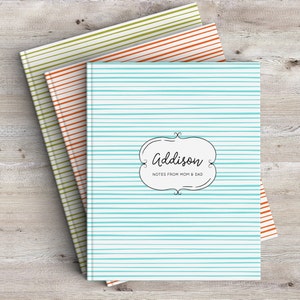 May include: Three striped notebooks stacked on top of each other. The top notebook is light blue with white stripes and says "Addison" and "Notes from Mom & Dad". The middle notebook is orange with white stripes. The bottom notebook is green with white stripes.